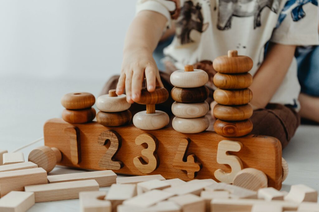 Un jeune enfant joue avec des blocs de bois en se concentrant intensément. Cette activité s'aligne sur les principes de l'éducation Montessori, favorisant l'apprentissage autonome et le développement de la motricité fine dès le plus jeune âge. 